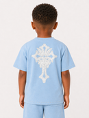 A child viewed from the back wearing a light blue short-sleeve T-shirt with a large white ornamental cross graphic on the back, paired with matching light blue pants, against a plain light background.