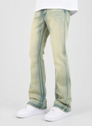 A person wearing light-wash blue-green denim jeans with a faded yellow-green tint and white sneakers, shown from the waist down against a plain light gray studio background.