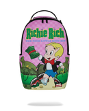 A sprayground backpack available at fresh n fitted featuring a colorful graphic print of the 'Richie Rich' cartoon character on a pink checkered background, with green title text and an illustrated scene of money bags and a shark.
