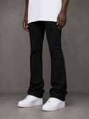 A person wearing black flare jeans with small silver speckles, styled with a white t-shirt and white platform sneakers against a textured gray studio background.