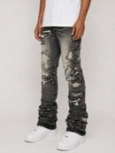 A person wearing heavily distressed and ripped black denim jeans with a faded gray wash, styled with a white t-shirt and white sneakers against a light gray studio background.