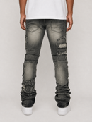 Rear view of a person wearing heavily distressed faded black denim jeans with ripped details and gathered cuffs, paired with a white t-shirt and white sneakers, against a light gray studio background.