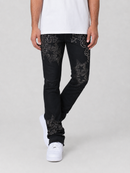 A person wearing black jeans with silver star and dot embellishments, paired with a white t-shirt and white sneakers, shown from the waist down against a light gray studio background.