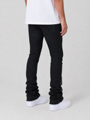 A person shown from the waist down wearing black slim-fit jeans with ruched detailing at the cuffs and white sneakers against a light gray studio background.