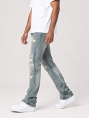A person wearing light-wash distressed denim jeans with ripped details, styled with a white t-shirt and white sneakers against a light gray studio background.