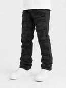 Black heavily distressed and ripped jeans with frayed details, shown on a model wearing a white t-shirt and white sneakers against a light gray background.