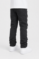 Rear view of a person wearing black distressed jeans with frayed edges and side details, paired with a white t-shirt and white sneakers, on a light gray studio background.