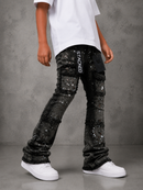 A child wearing black sequined cargo pants with white 'STACKED' branding down the side, styled with a white t-shirt and white sneakers against a gray textured studio background.