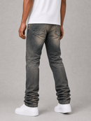 Rear view of a person wearing dark gray washed denim jeans with a white t-shirt and white sneakers, standing against a neutral gray studio background.