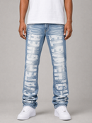 A person wearing light blue distressed denim jeans with large white vertical text graphics down both legs, paired with a white t-shirt and white sneakers, photographed against a neutral gray studio background.