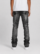 Rear view of a person wearing dark gray heavily distressed and embellished jeans with silver studs and drawstring details, paired with a white t-shirt and white sneakers, on a light gray studio background.