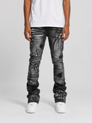 A person wearing distressed black and gray denim jeans with metallic rivet embellishments, paired with a white t-shirt and white sneakers, shown from the waist down on a light gray studio background.