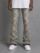A person wearing patterned beige and gray flared jeans with a white t-shirt and white sneakers, standing against a gray textured studio background.