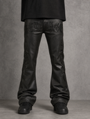 Black leather flare jeans with raised gothic-style embroidery on the back pockets and down the sides, shown on a model from the waist down against a textured gray studio background.