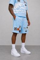 A model wearing a light blue and white Manchester City themed athletic tracksuit with various sponsor patches, white crew socks, and white sneakers, set against a neutral gray studio background.